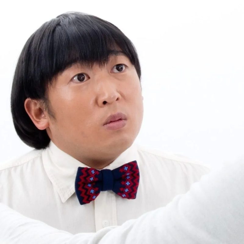 男性が蝶ネクタイと白いシャツを着て、見上げている写真です。