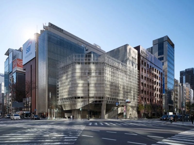 晴れた日の街並みの写真。交差点に面した複数の高層ビルが写っています。左側のビルには「SBI Shinsei Bank」の看板があり、その上のビルには「HERMES」の文字が見えます。右側のビルには「SONY」の文字が見えます。横断歩道を歩く人々や、車も写っています。