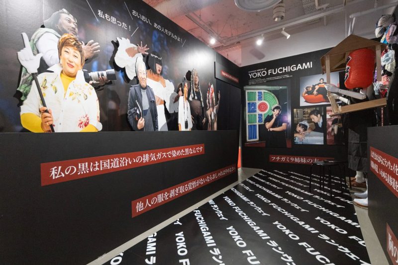 展示会場の様子。壁には様々な人物の切り抜きが飾られ、床には「YOKO FUCHIGAMI」の文字がデザインされたマットが敷かれている。