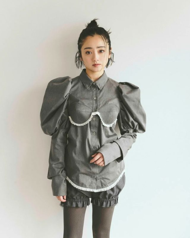 女性がグレーのシャツとショートパンツを着て立つスタイリング