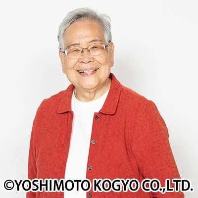 笑顔の高齢女性のポートレート。彼女は眼鏡をかけ、赤いジャケットを着ている。