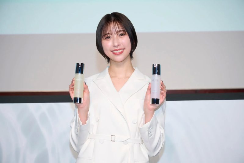 白い服を着た女性が、化粧品のボトルを2つ持って微笑んでいる写真