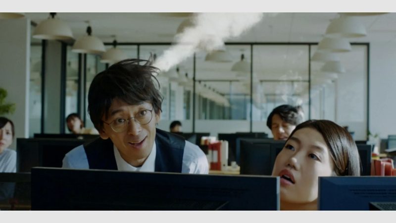 オフィスで働く人々の様子を捉えた写真。驚いた表情の女性と、それを見ている男性、そして煙のようなものが写っている。