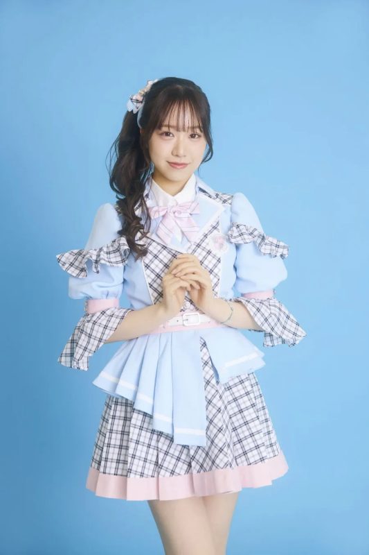 水色の衣装を着た女性のポートレート。彼女は髪をポニーテールにし、ピンクのリボンで飾っています。背景は水色です。