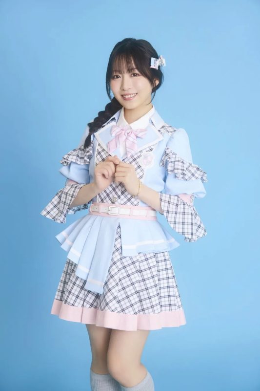 水色の衣装を着た女性のポートレート。彼女は笑顔で、髪は三つ編みで、リボンとヘアピンで飾られています。背景は単色です。