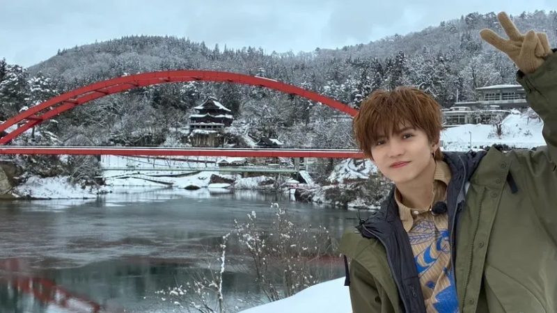 雪景色の中、赤い橋の前でピースサインをする佐藤大樹さん