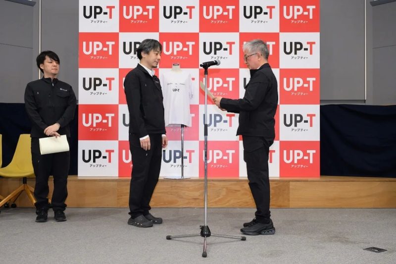 プレゼンテーションをするひろゆき氏とUP-Tのロゴ
