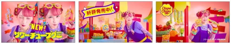 チュッパチャップスのCM。ピンクの髪の女性が、サワーチューブグミやチュッパチャップスなどの商品を持っている。背景にはお菓子屋さんやフルーツが並んでいる。