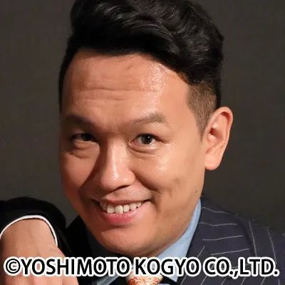 笑顔を見せる男性のポートレート。彼は黒い髪型で、ストライプのジャケットを着ている。