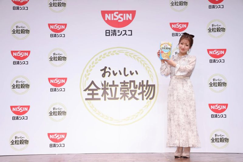女性が「日清シスコ」の「おいしい全粒穀物」のパッケージを持って立っている写真です。
